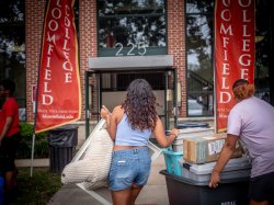 Student carrying pillow and frame walking toward Franklin Residence Hall between Bloomfield College flags