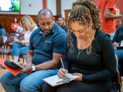 Two parents sitting next to each other, writing a letter on a clipboard