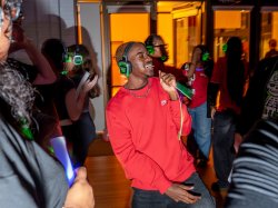 Student in long-sleeve red shirt singing while holding glowsticks and wearing headphones at the silent disco